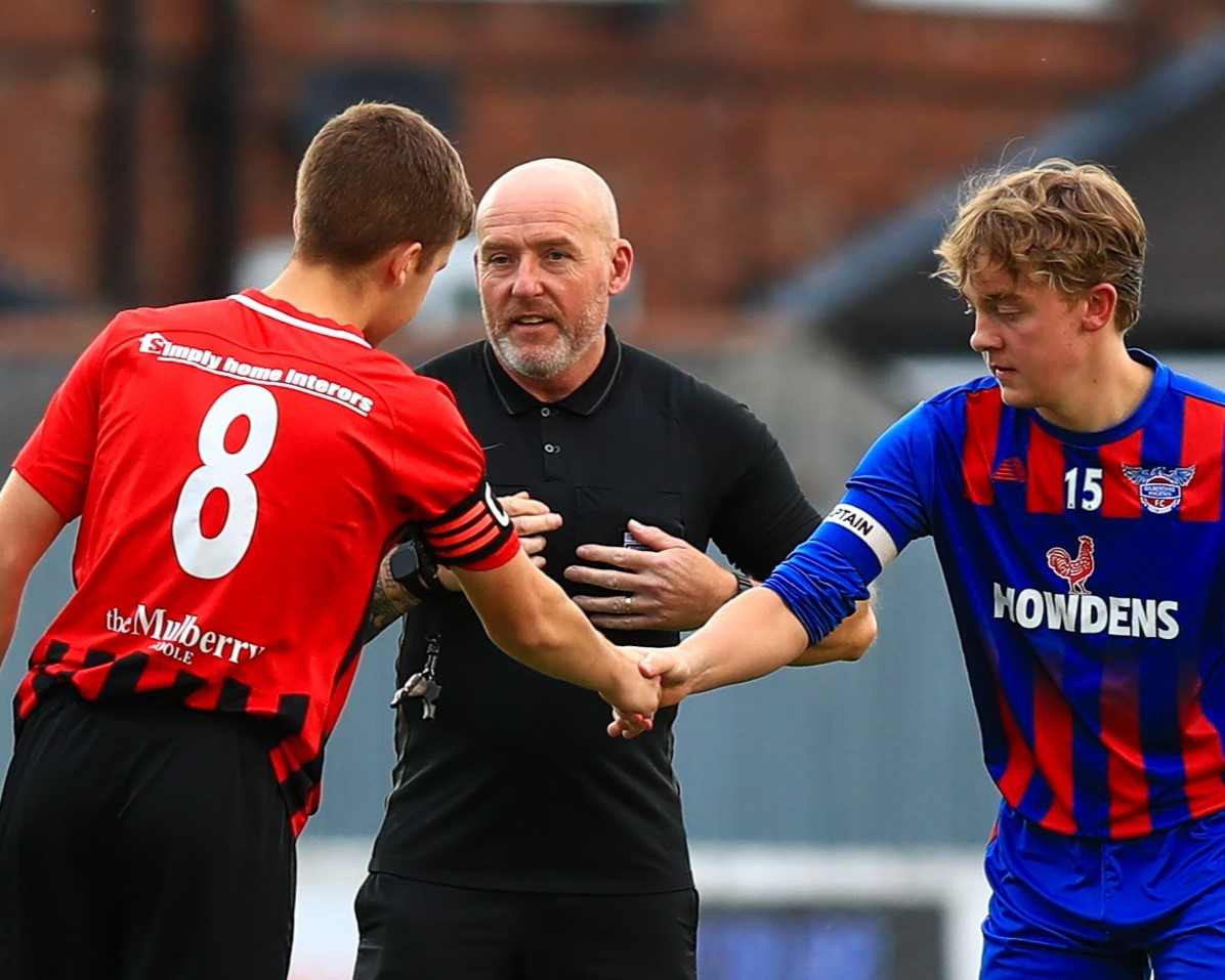 Two footballers shaking hands in front of a referee